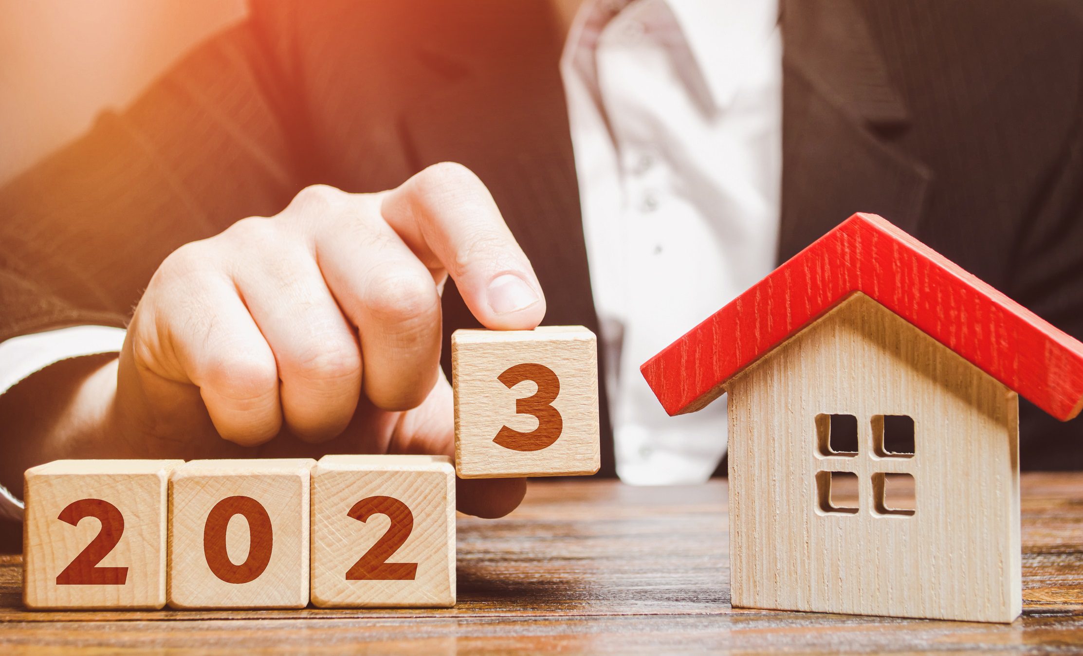 A businessman stacks blocks spelling out "2023" near a miniature wooden house for marketing tips for loan officers blog.